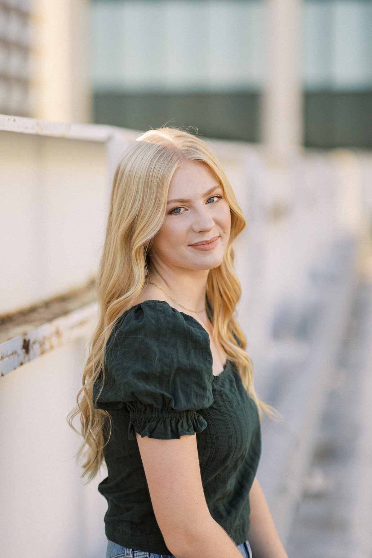 young blonde woman smiles at camera posing for senior photos in parking garage