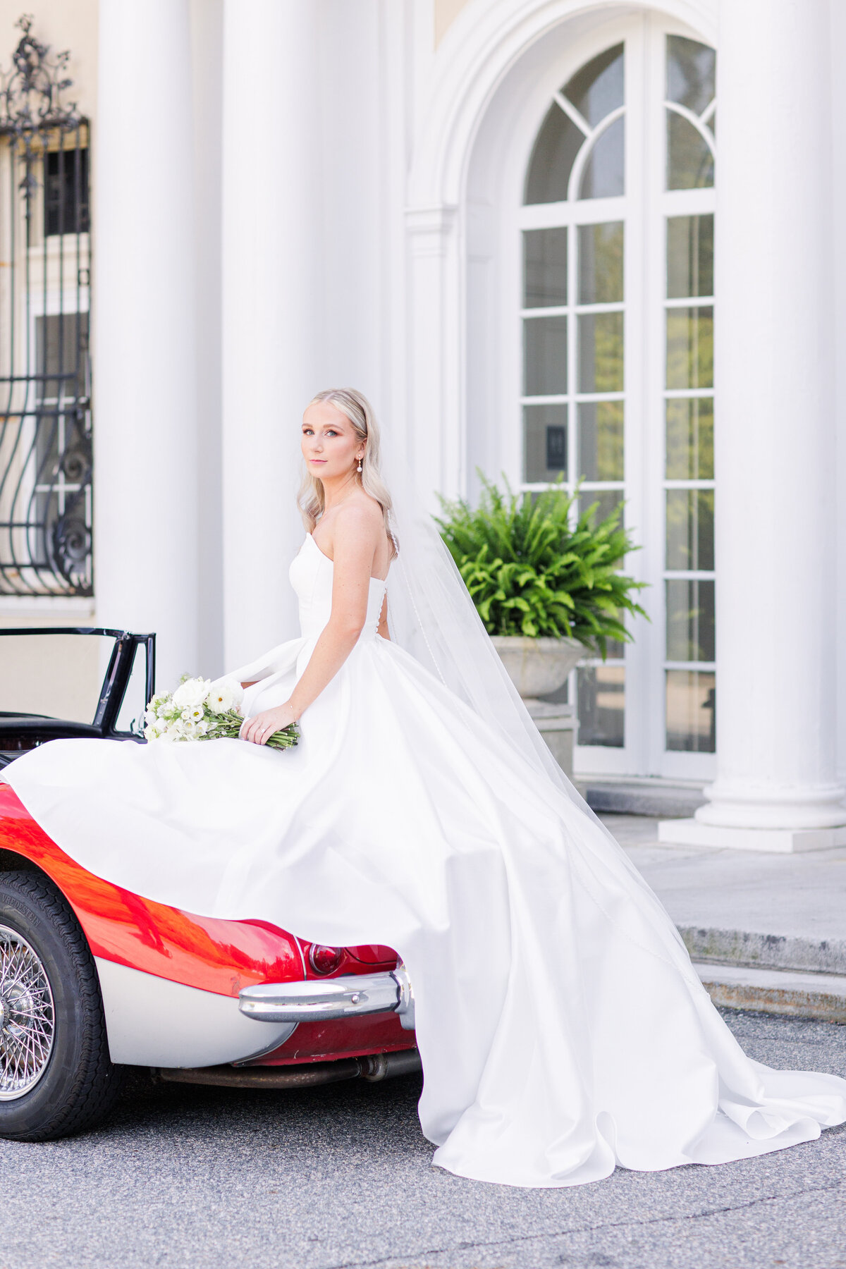 Bride sitting on an antique car in front of Tupper Manor representing editorial Boston wedding photography