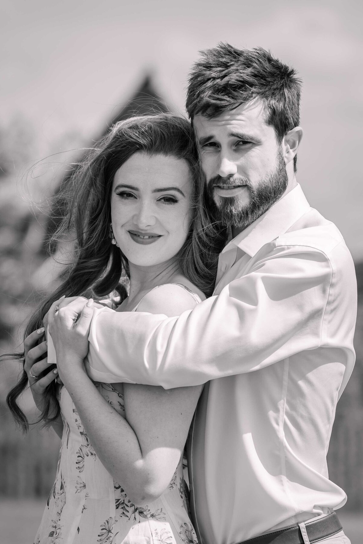 A black and white photo of an engaged couple hugging and smiling at the camera