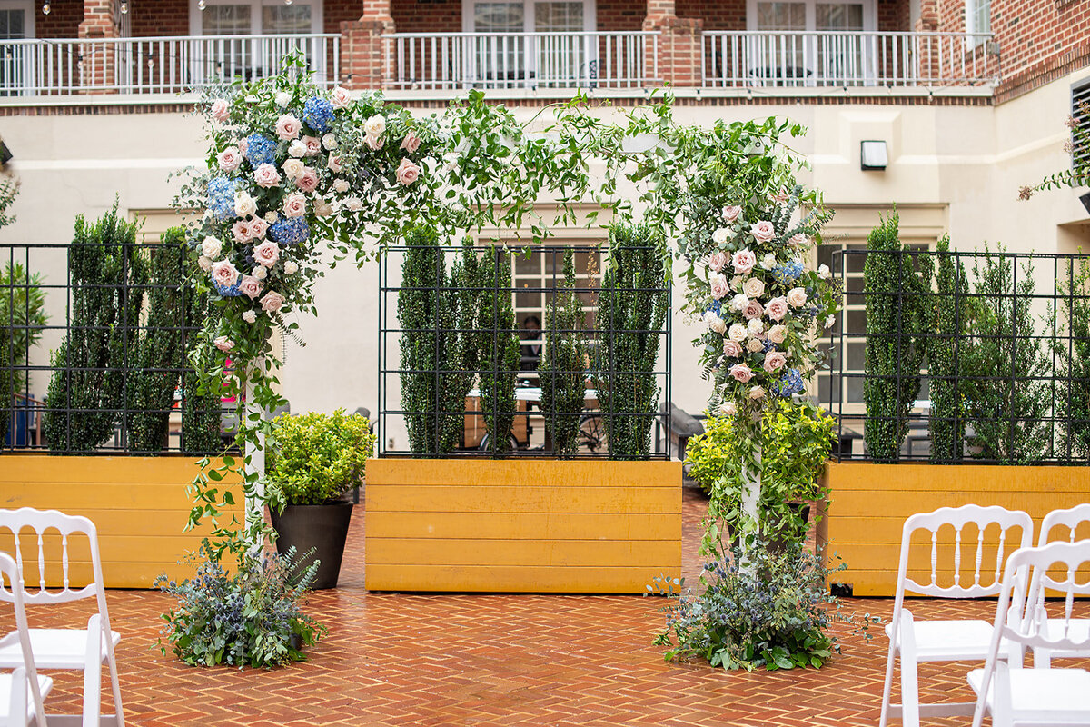 Colorful ceremony backdrop with lush floral arrangements featuring roses and greenery in the sunny courtyard of The Alexandrian  in Virginia..