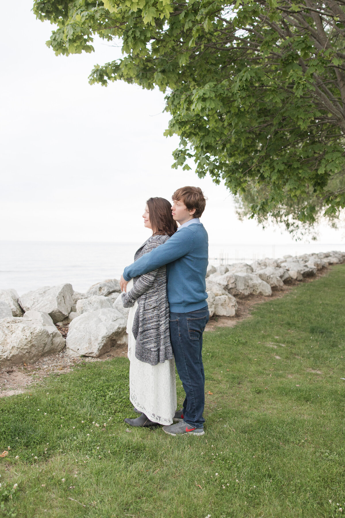Expectant couple holding each other and looking out at the lake