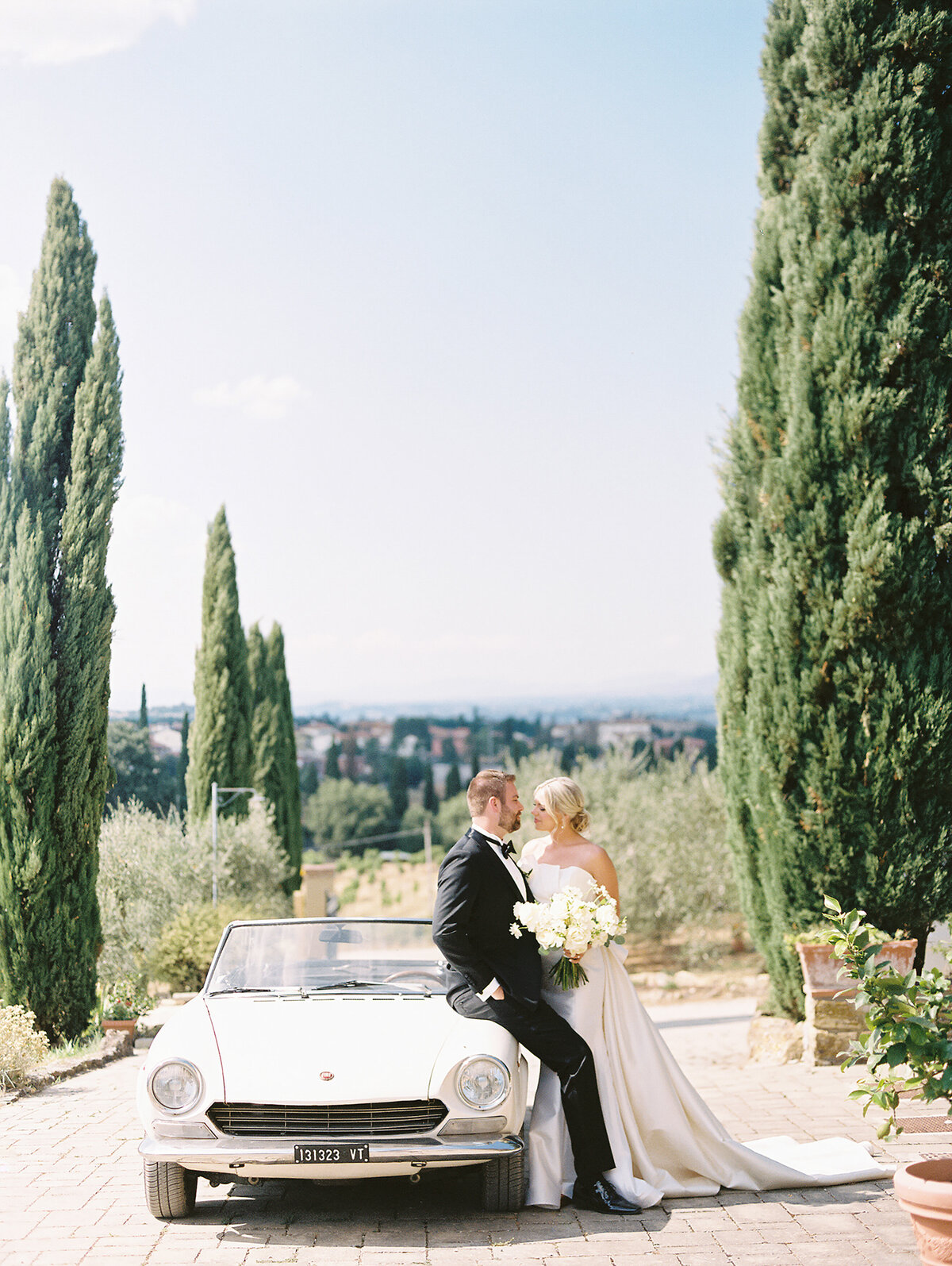 Bride and groom embracing and leaning on a car photographed by Chicago editorial wedding photographer Arielle Peters