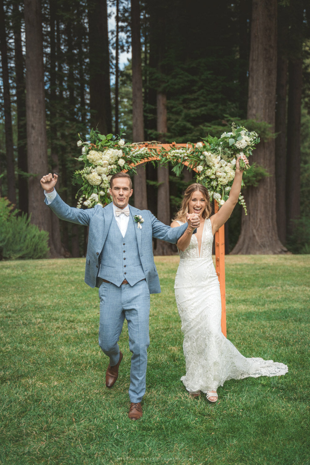 Bride and groom celebrating under rustic greenery wedding arch outdoors