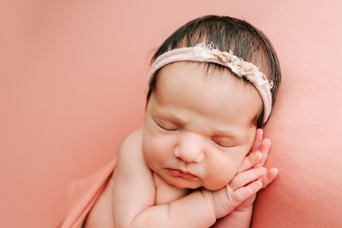 portrait of newborn girl sleeping on a coral blanket with her hands under her cheeks