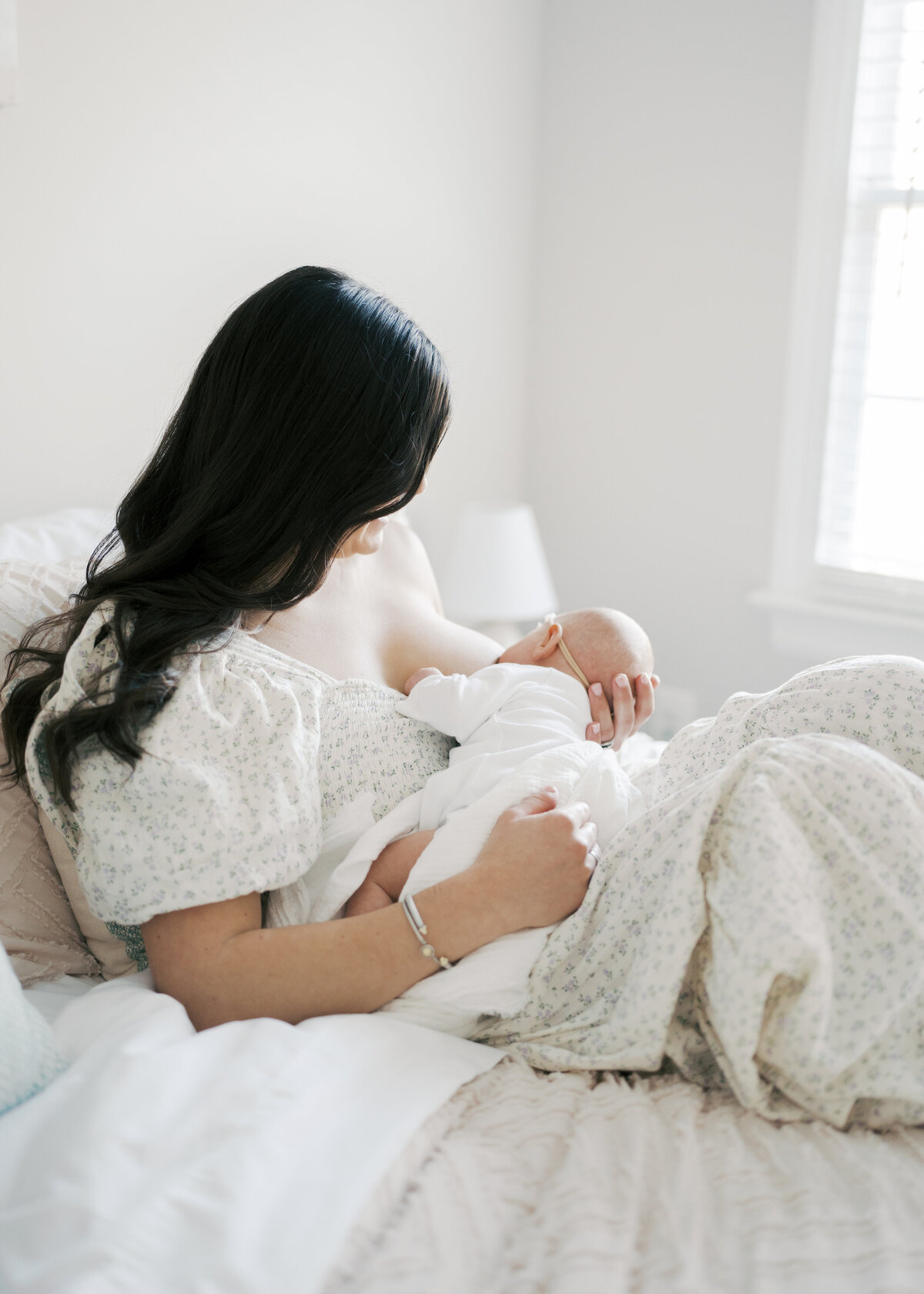 Women nursing newborn baby while laying on bed in Virginia Beach newborn session