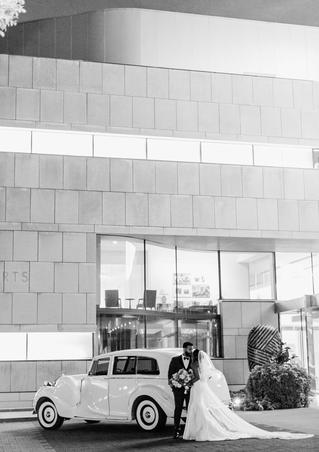 bride and groom kiss with car