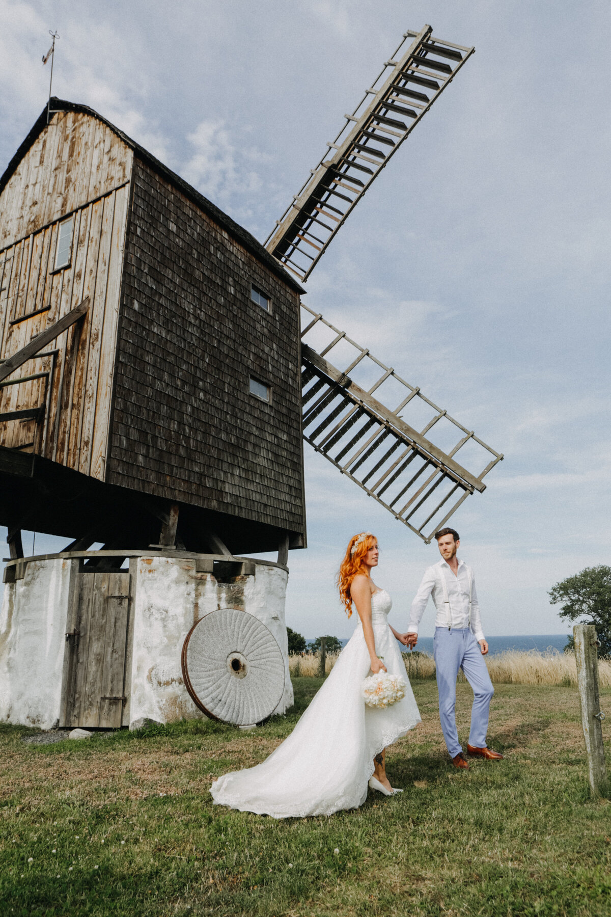 A couple by the old mill during their adventure elopement wedding abroad to Bornholm