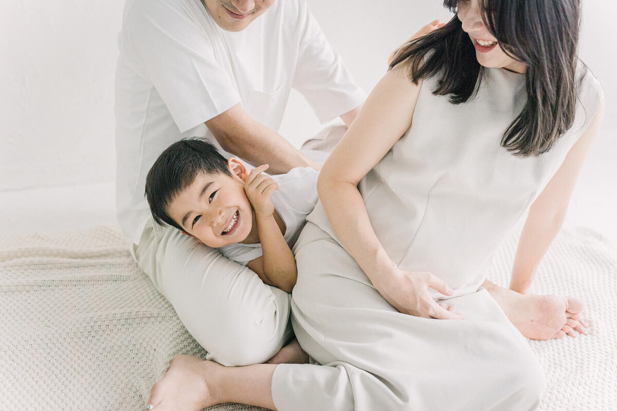 男の子が、ママとパパの膝の間でじゃれて笑っている、可愛らしいマタニティフォト。新宿のスタジオでYukika Ishikawa Photographyが撮影。