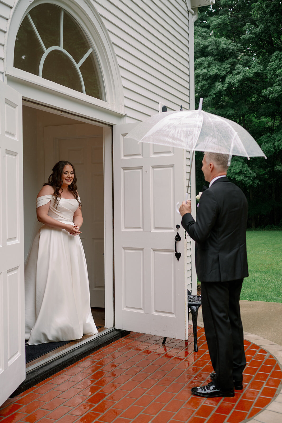 Bride stepping out of The Morris Estate chapel while her dad holds an umbrella on a rainy Michigan wedding day.