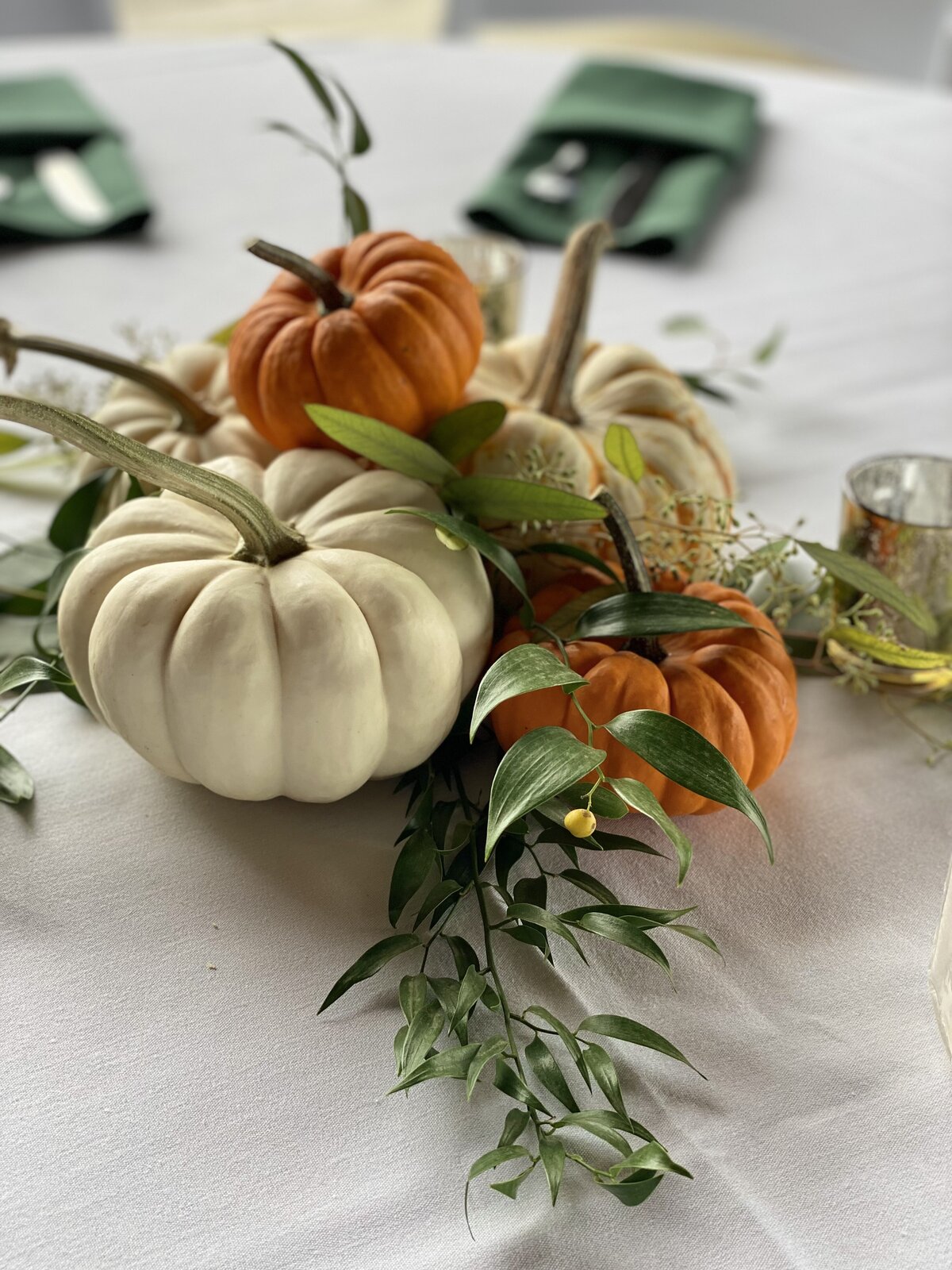 White and orange pumkins with green foliage on the reception tables.