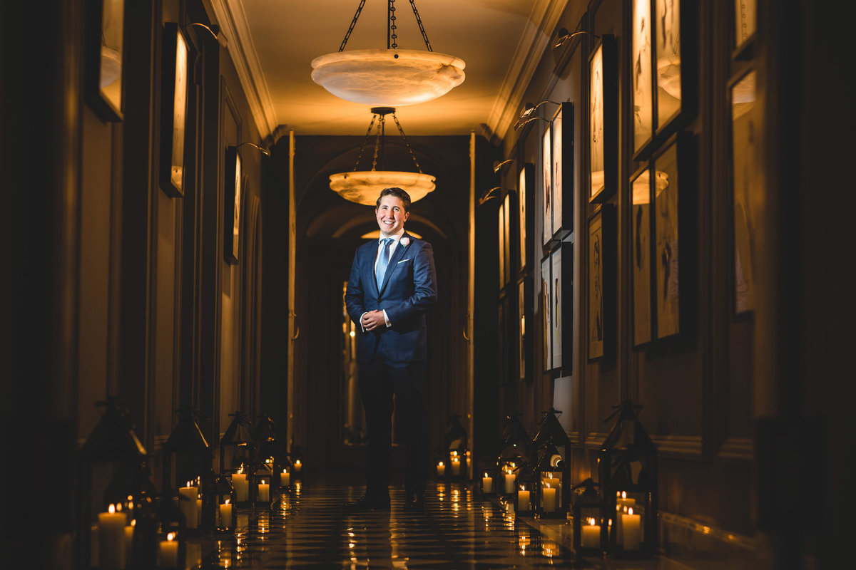 A portrait photograph of a groom stood in the hallway at Claridges