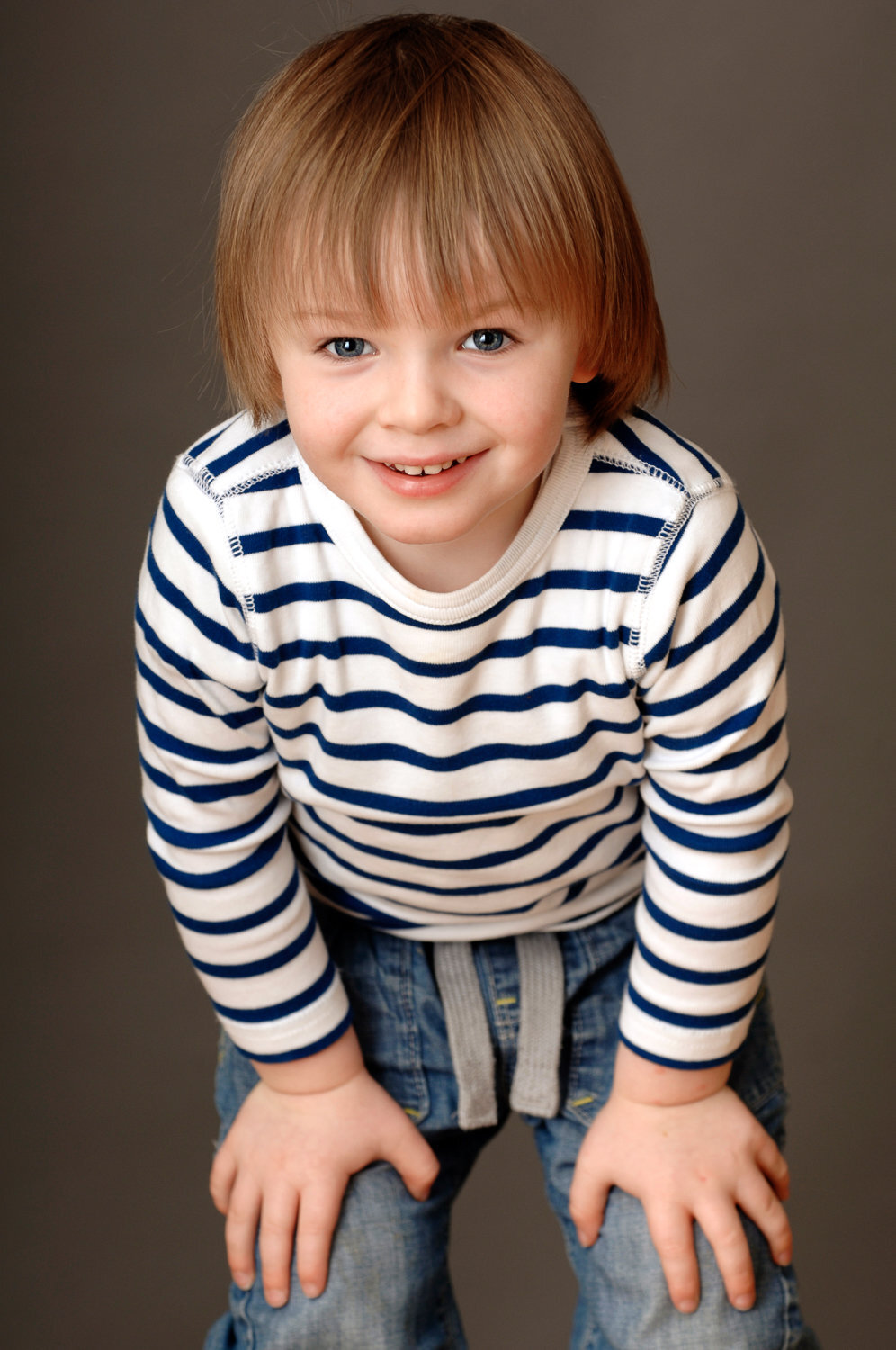 toddler boy with brown hair, wearing top with stripes and jeans smiling
