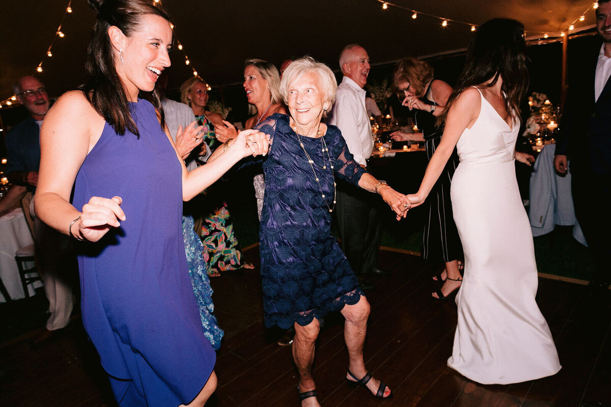 The bride and an old woman, with other guests, are dancing in Cape Cod Summer Tent, MA.
