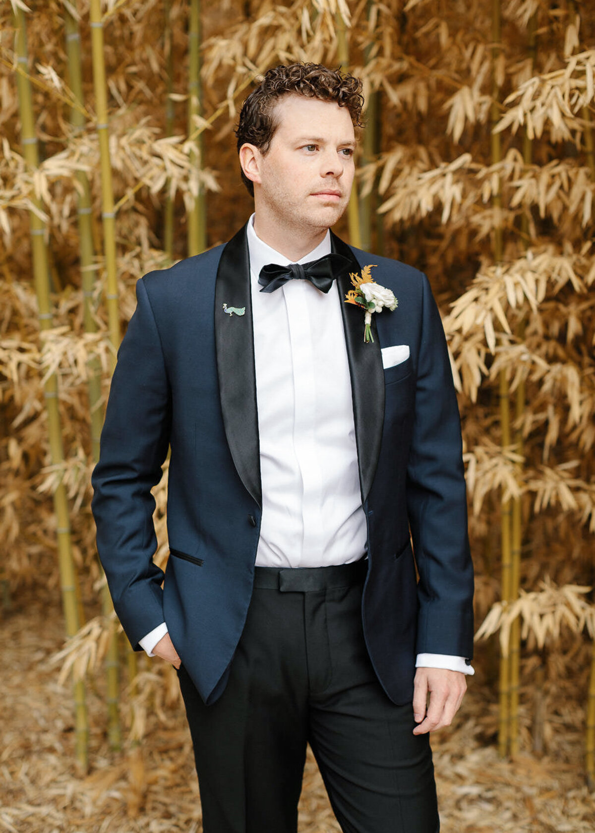man in blue tuxedo bow tie in front of golden plants groom