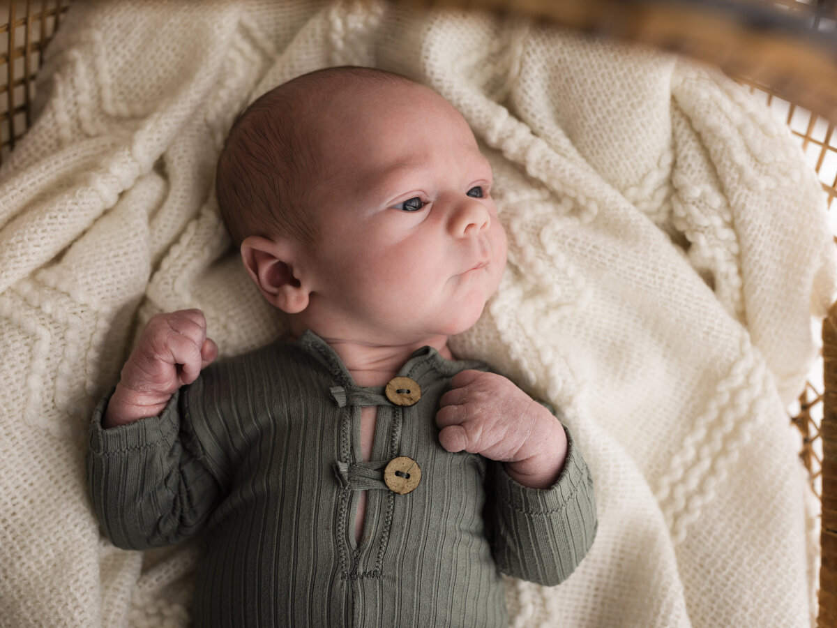 newborn baby boy in green onesie laying in bassinet