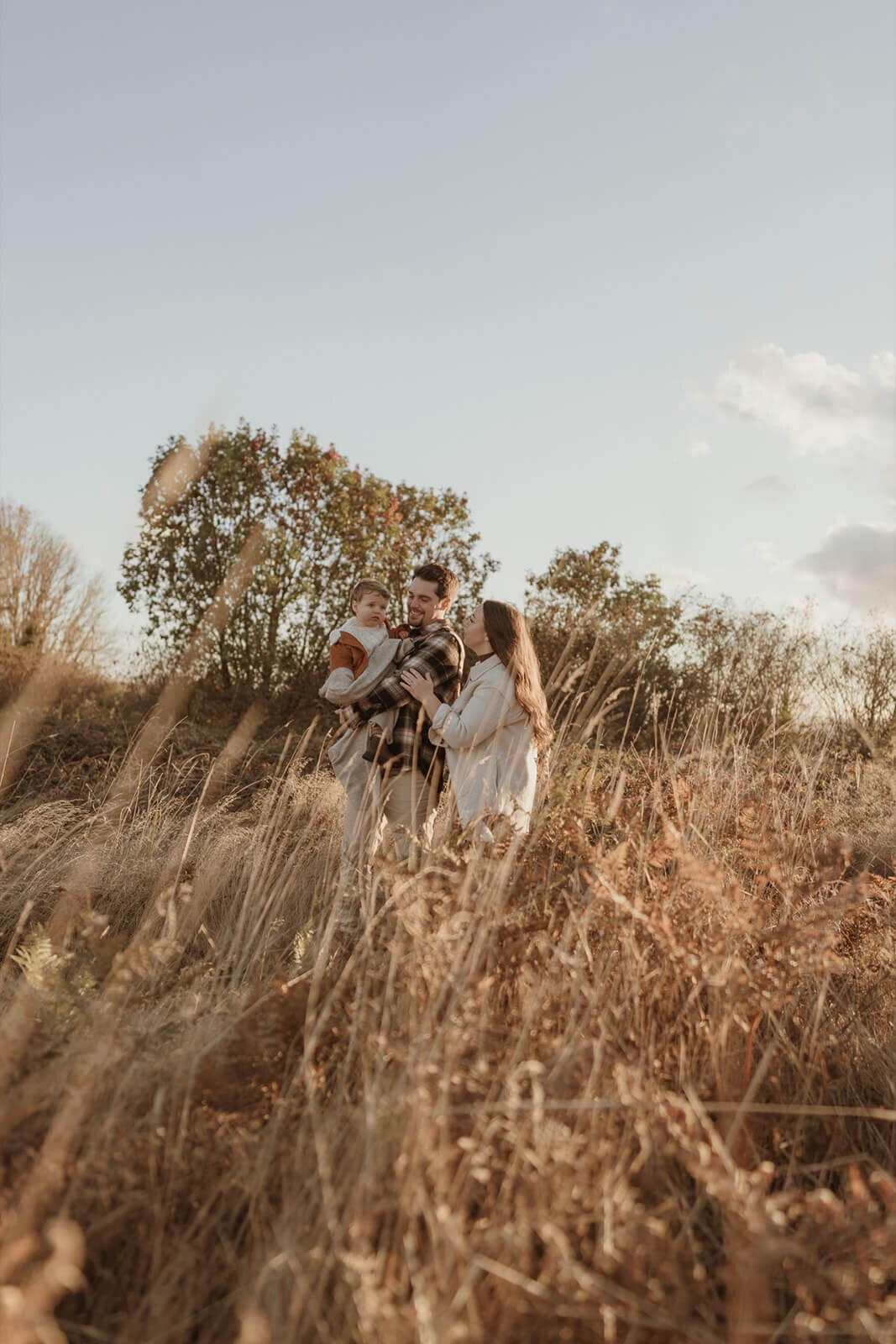 male and pregnant female walking with toddler in golden hour light at park with tall grass