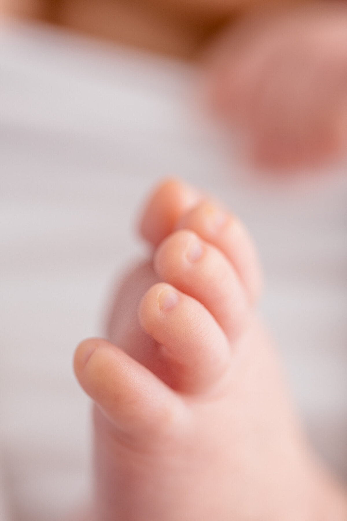 Close-up of a babys foot with tiny toes curling slightly. The soft, delicate skin is clearly visible, set against a blurred background.