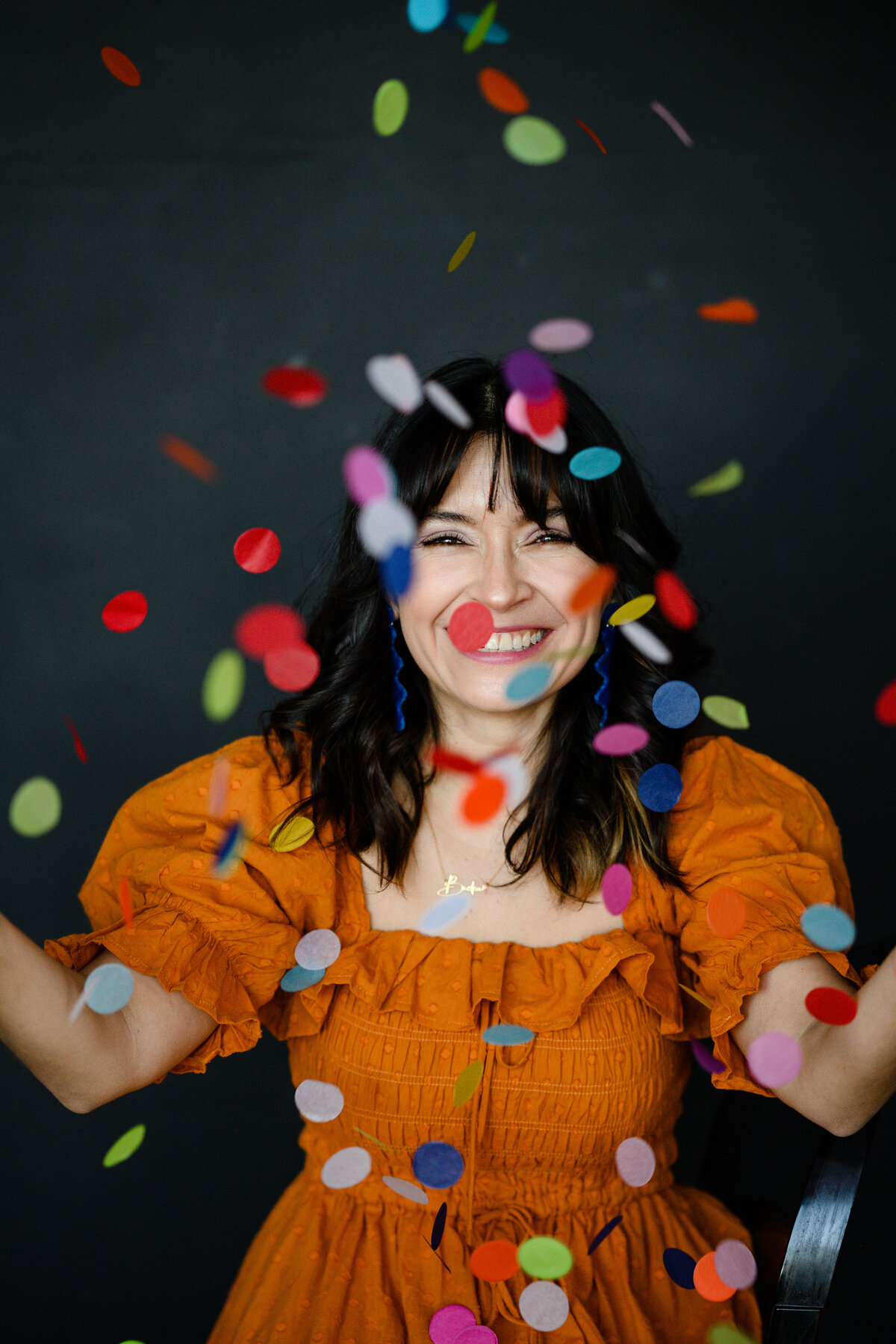 A brand photographer in Denver takes photos of a woman in an orange dress tossing little bright papers of confetti during her brand photos for her branding photo shoot in Denver.