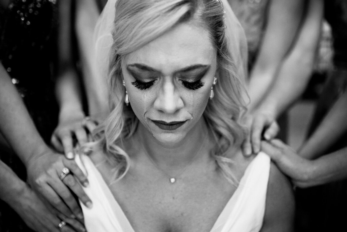 Close-up headshot of the bride with tears in her eyes, while hands of some people holding her. Image by Jenny Fu Studio