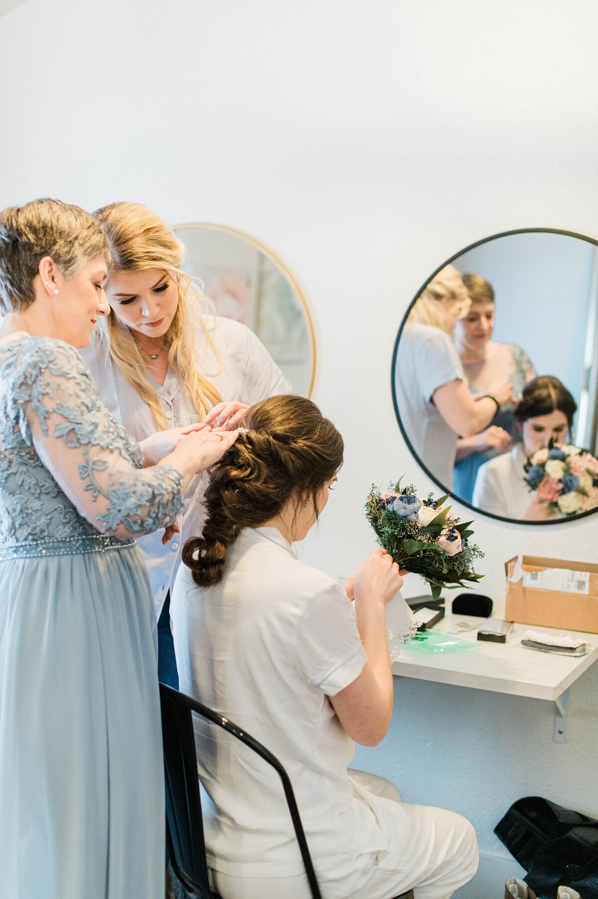 A bride touches up her blue and green bridal bouquet while her hair gets final touches as she sits in her bridal suite at Boulder Wedgewood
