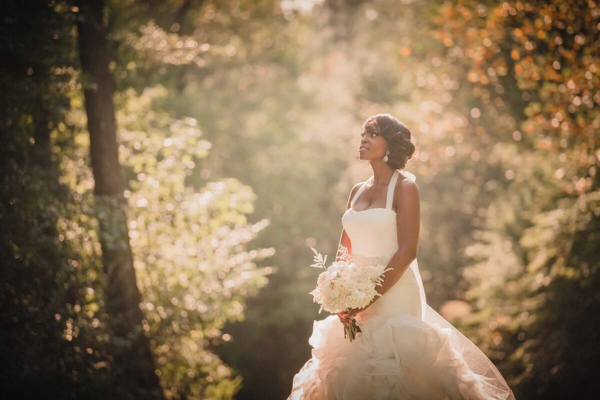 A bride standing in a wooded area holding a bouquet