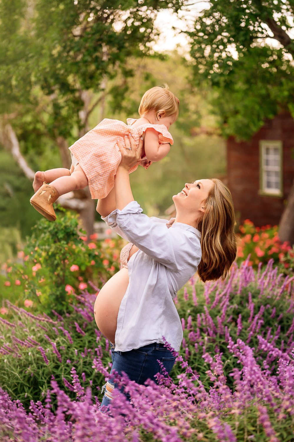 pregnant mama lifts her baby. her shirt is unbuttoned showing her pregnant belly