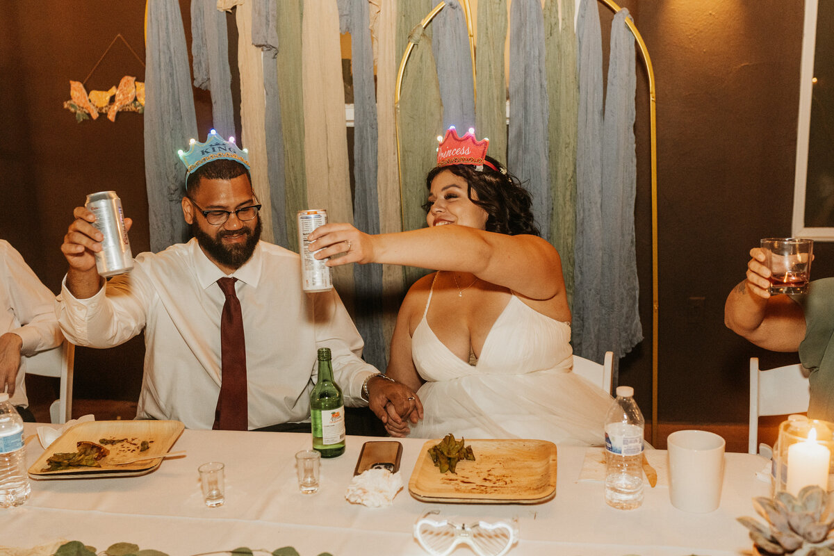 A wedding couple wearing small crowns and smiling 