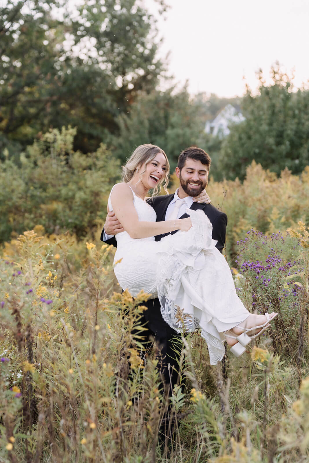 Groom carrying bride through long grass