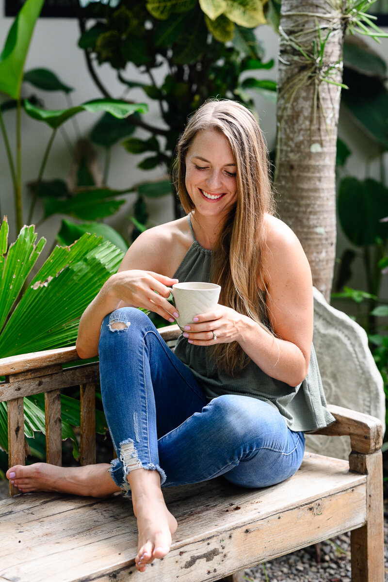 A personal branding photographer in Denver and commercial photographer in Denver takes a picture of a hormone health coach sitting on a bench holding a coffee cup and smiling for her brand photos by a branding photographer.