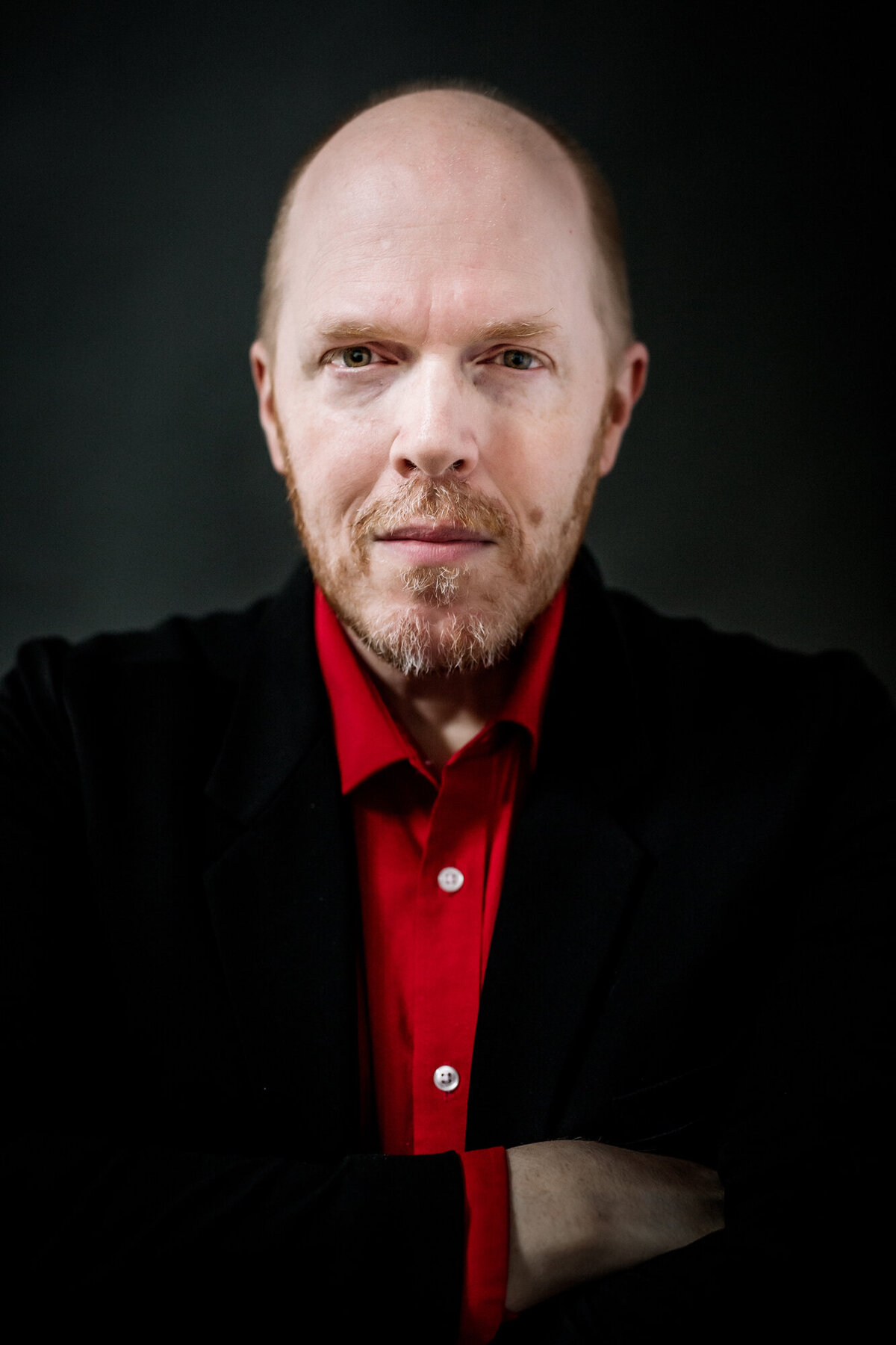 Male headshot client wearing a black suit & red shirt with a serious expression