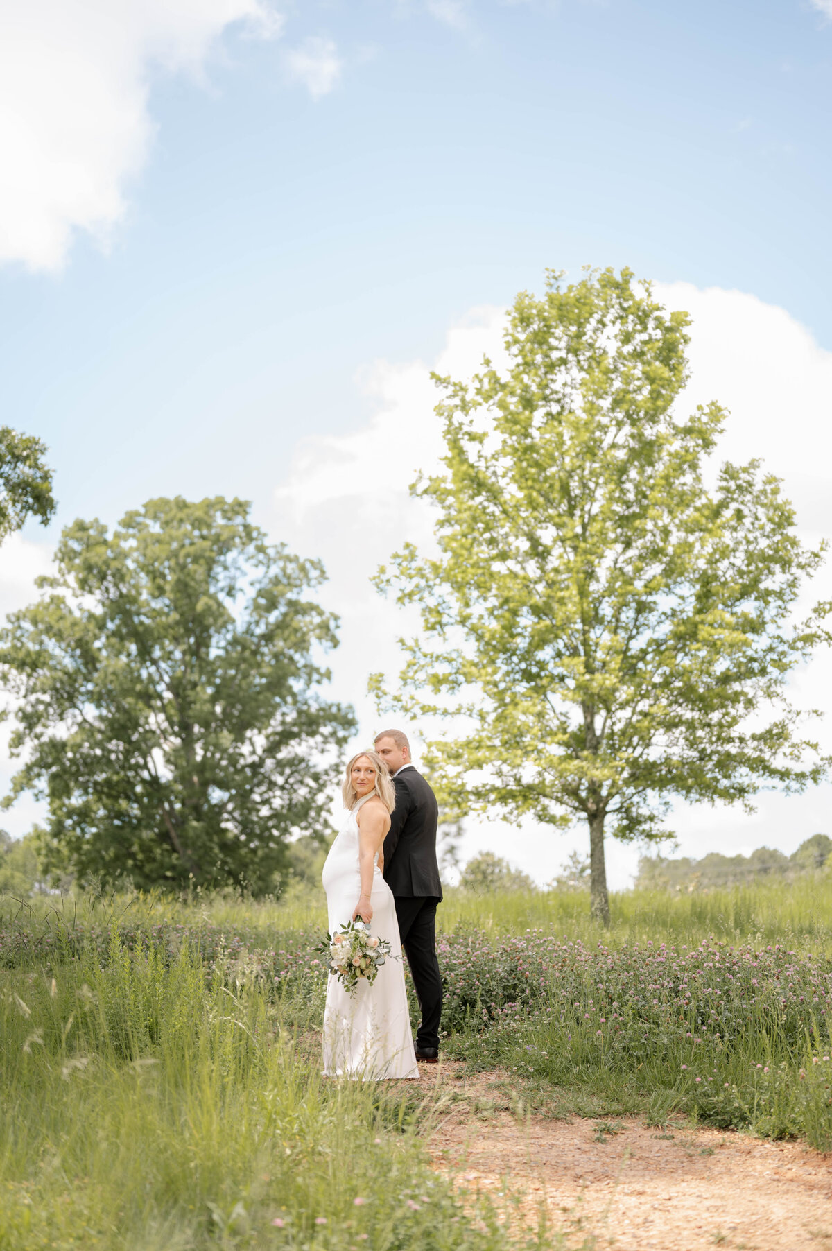 A bride poses in front of her bridal party, all wearing bright colors and holding white parasols.