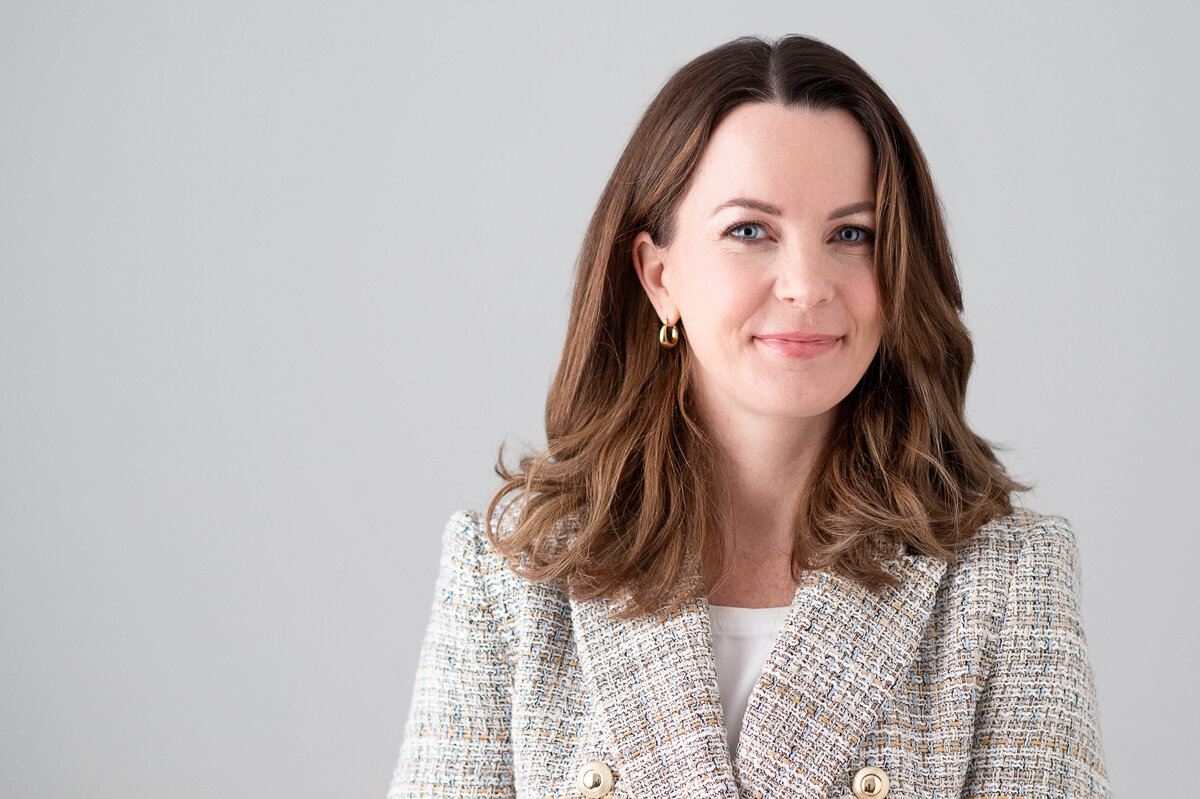 a classic studio headshot showing a brown haired woman wearing a tweed suit jacket against a white backdrop.  Captured in-studio by Ottawa Headshot Photographer JEMMAN Photography COMMERCIAL