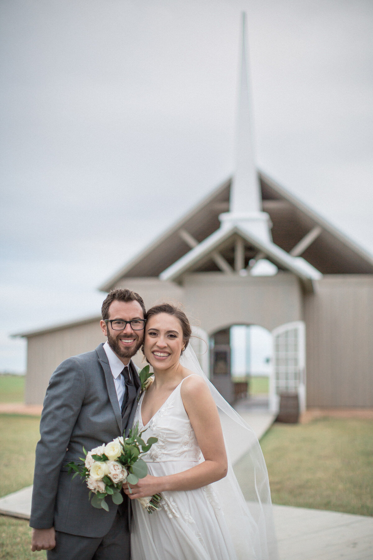 The bride and groom look straight into the camera outside of their wedding venue in Austin, Tx