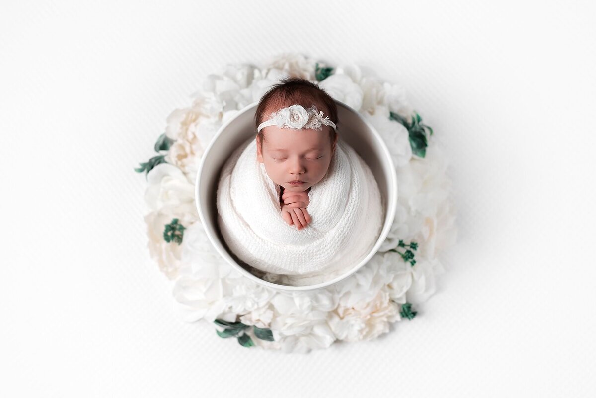 Newborn girl in white wrap posed in a bucket.