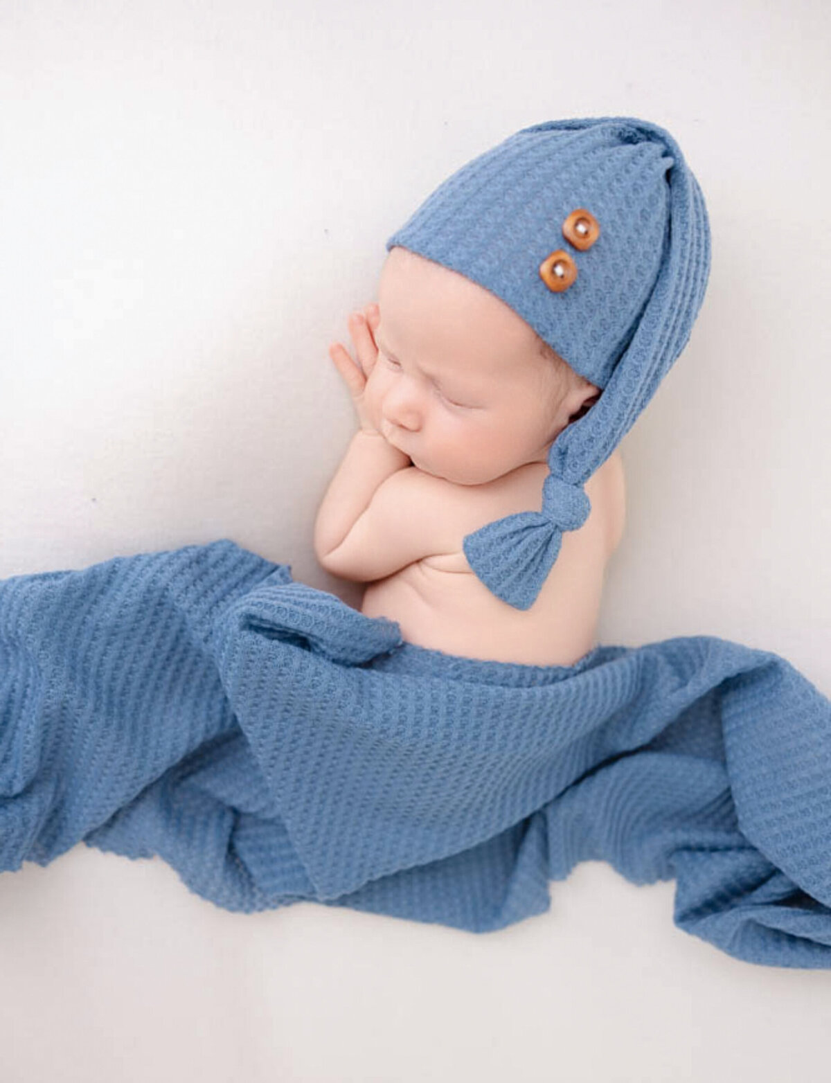 Newborn baby boy wearing a blue sleepy hat and matching blanket.