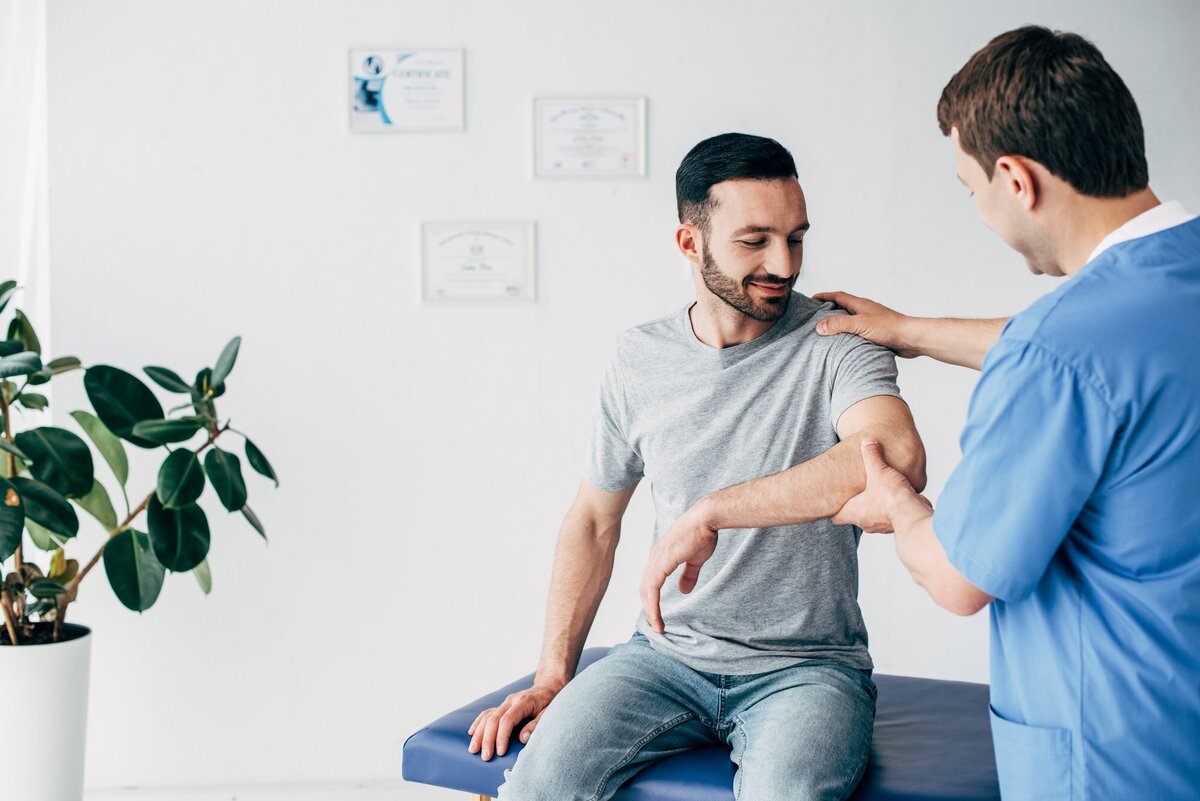 selective-focus-of-chiropractor-examining-patient-shoulder-in-massage-cabinet-at-clinic