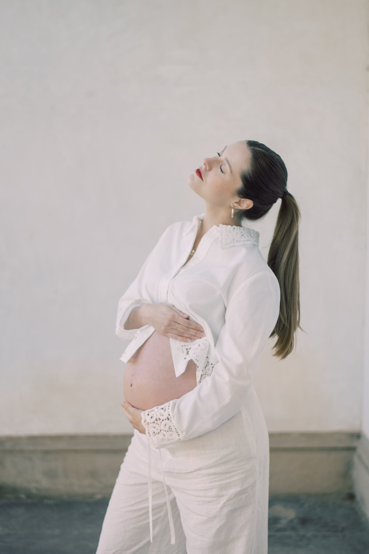 oyful maternity portrait of a woman gazing upward with hands on hips, sunlight highlighting her natural glow