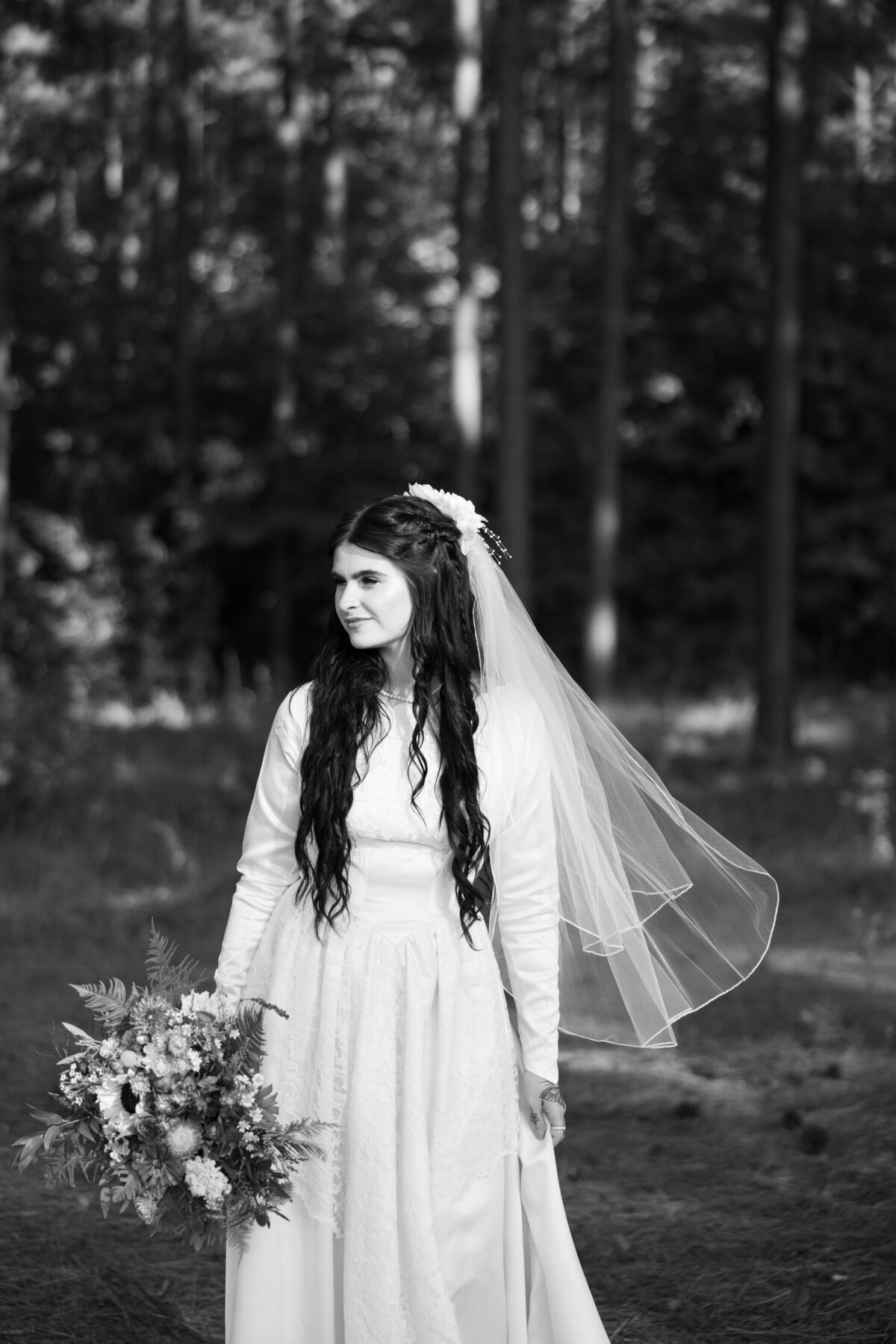 A bride standing in a wooded area looking off to the side and holding a bouquet of flowers