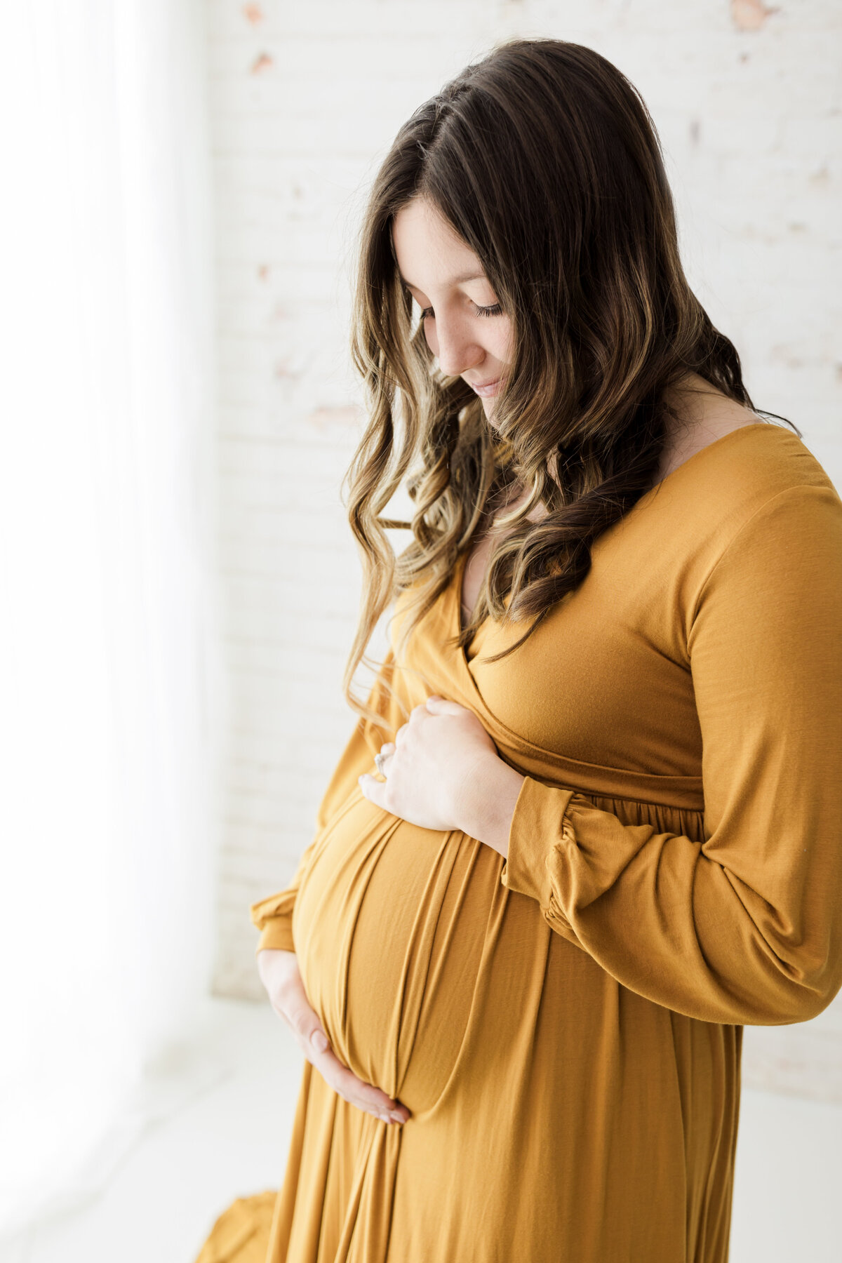 pregnant mother in gold maternity gown holding baby bump for studio maternity photoshoot