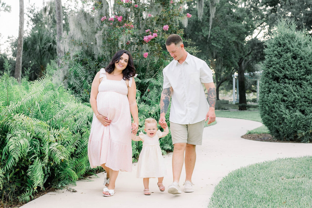 Pregnant couple walking with toddler in a park for a Tampa maternity photographer Tina Marie Studio.