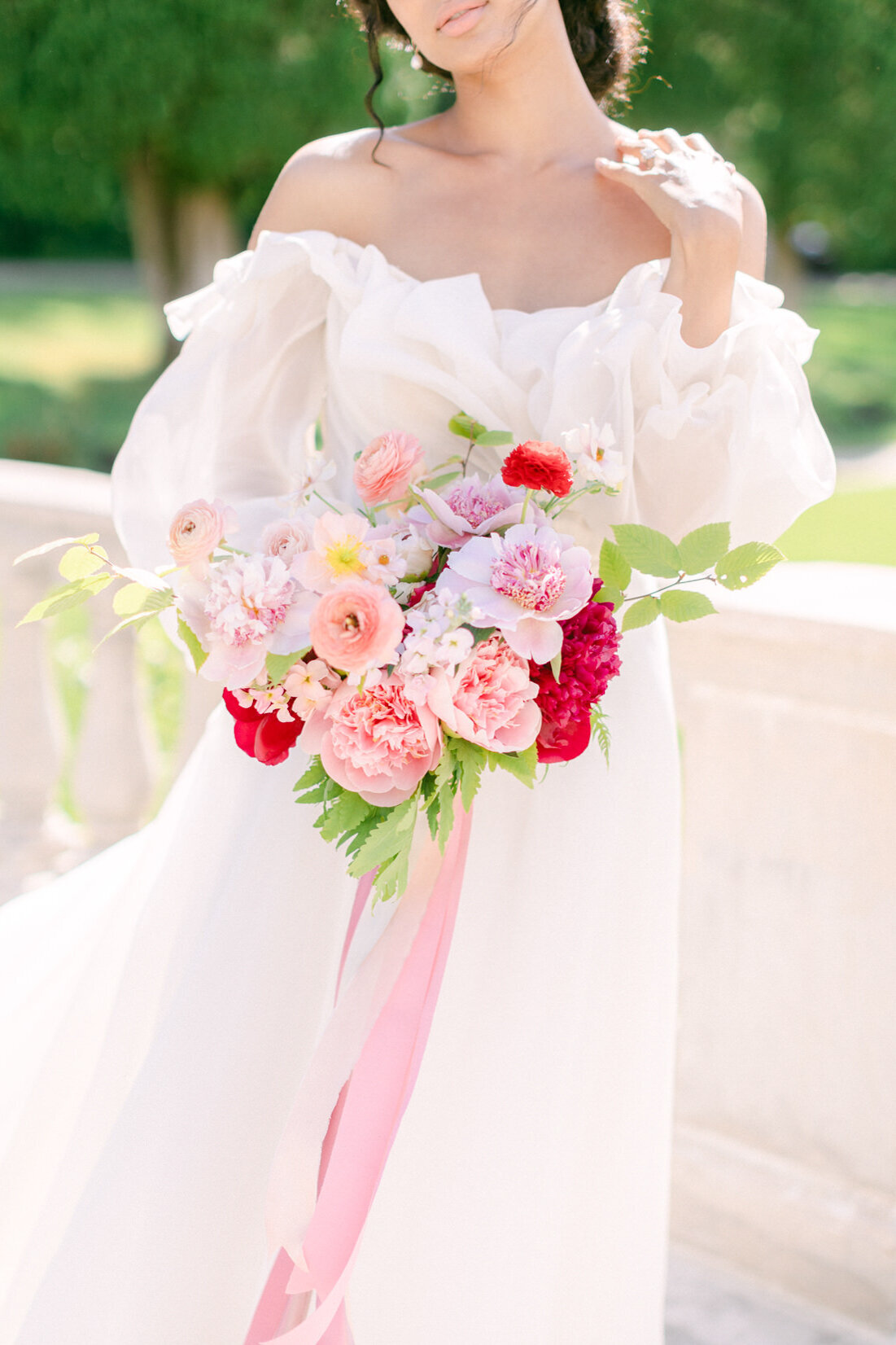 A bride holds a lush bouquet of pink and red flowers tied with ribbon at Stonehaven Manor.