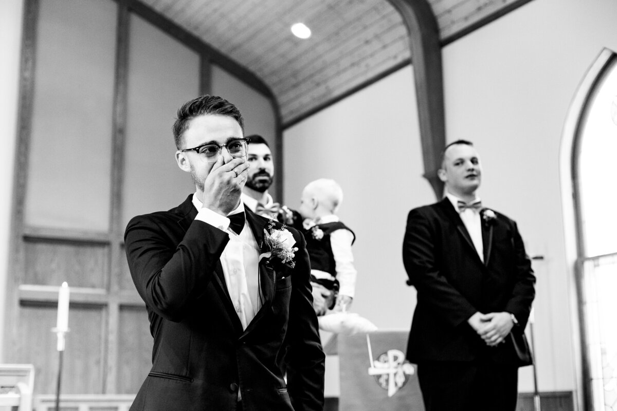 One of the top wedding photos of 2020. Taken by Adore Wedding Photography- Toledo, Ohio Wedding Photographers. This photo is of a groom covering his mouth and crying as the bride walks down the aisle at the wedding in Detroit Michigan