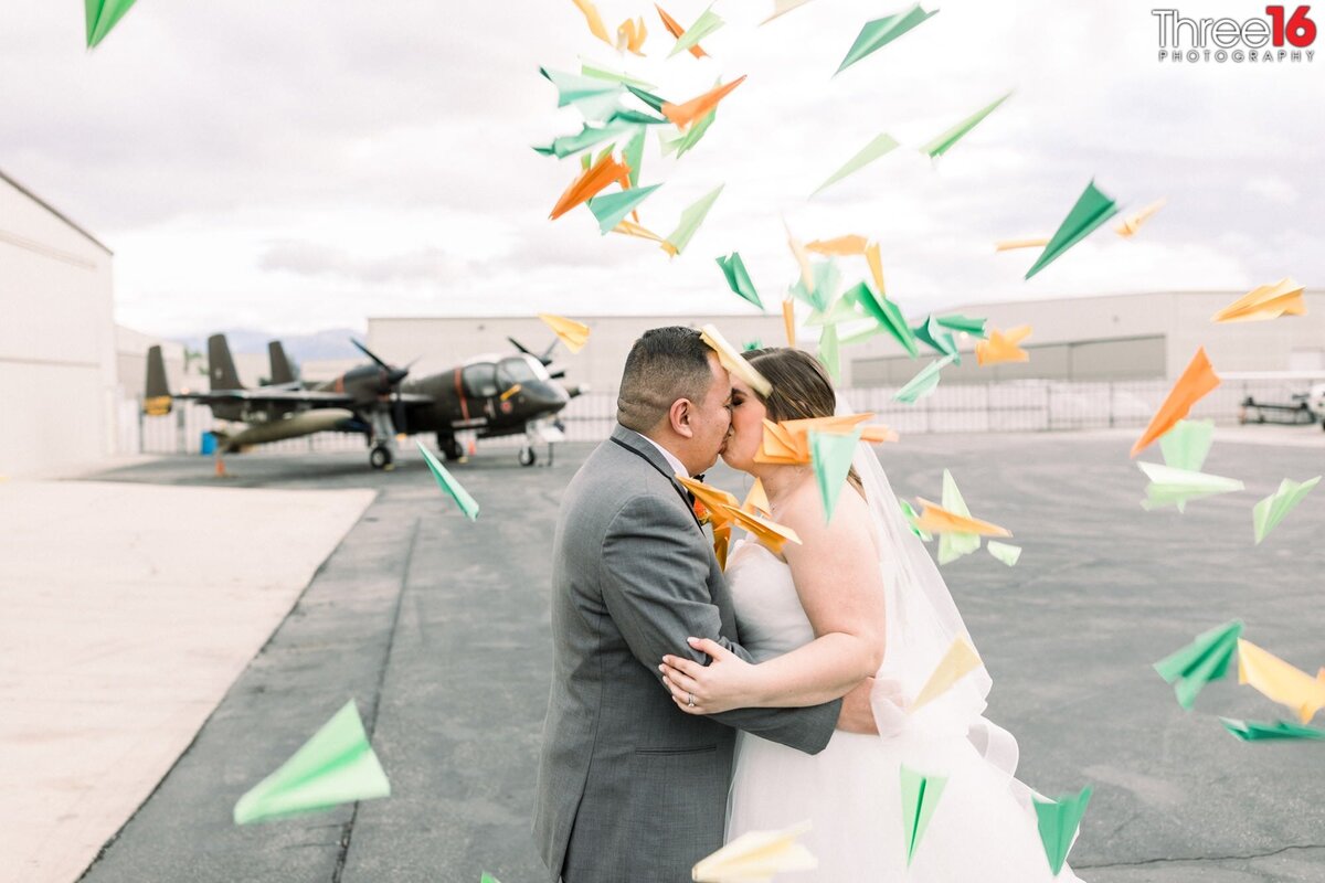 Bride and Groom share a kiss as wedding guests throw paper airplanes at them