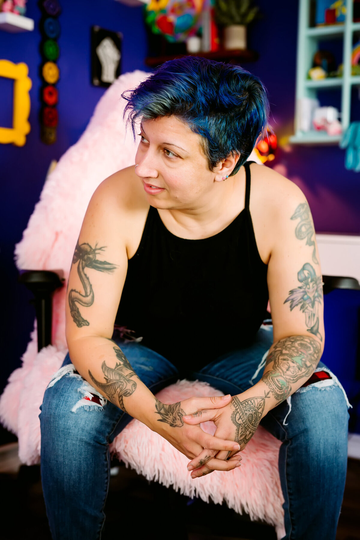 They/them podcaster sitting in a chair looking off to the side, leaning forward with hands clasped in a power stance, posing for a South Shore MA branding photographer