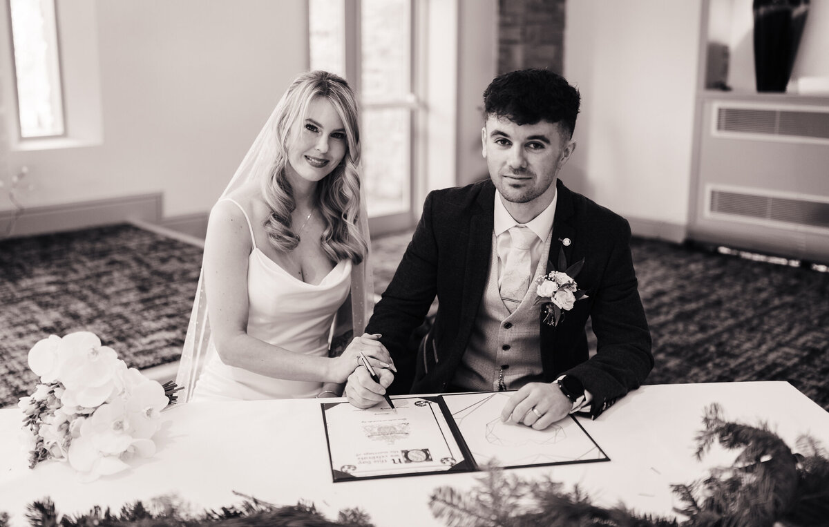 Black and white picture of bride and groom signing the register at Mytton Fold takne by documentary wedding photographer Anthony Horseman