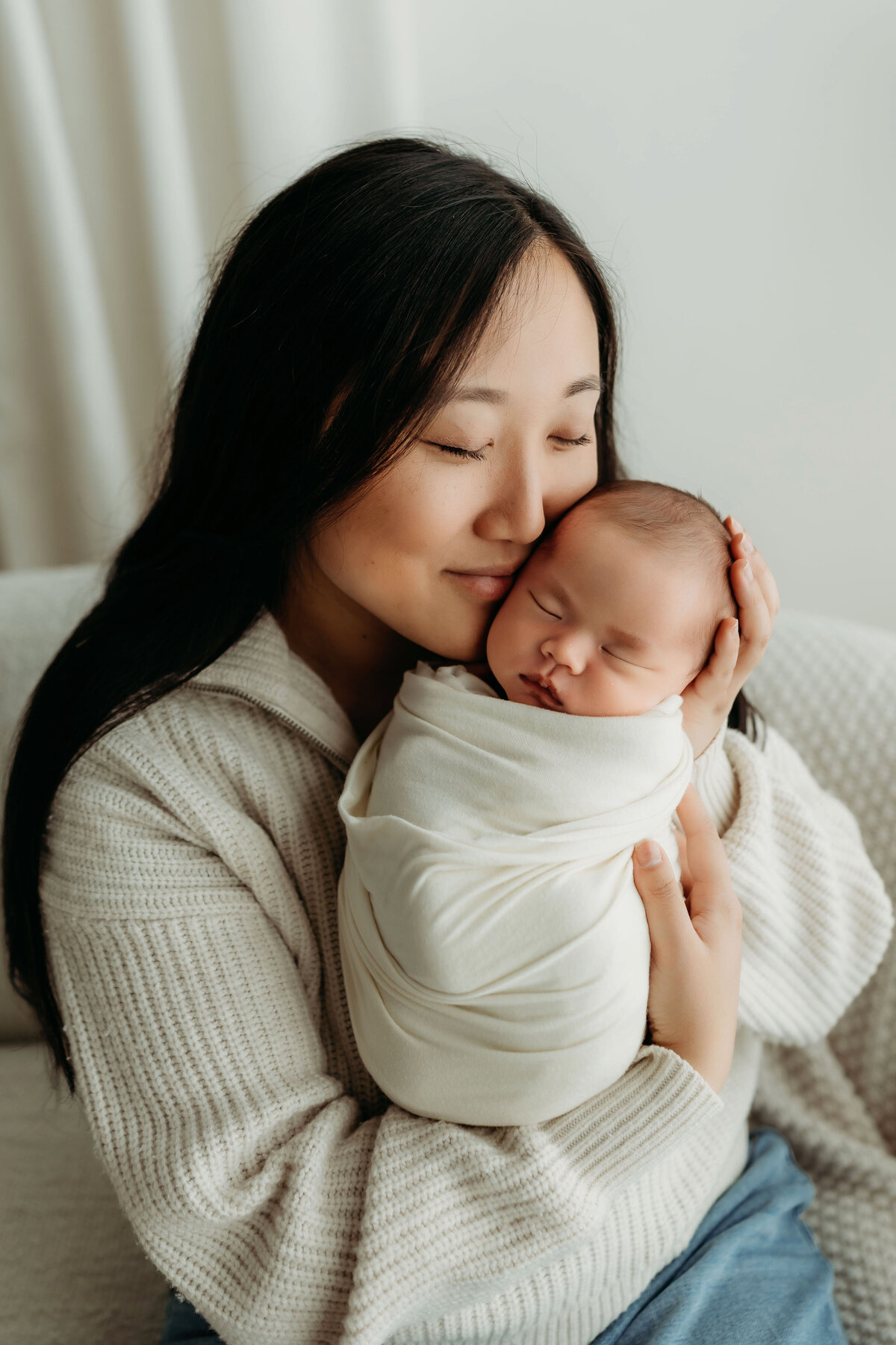 A mother cradles her newborn baby who is swaddled and sleeping