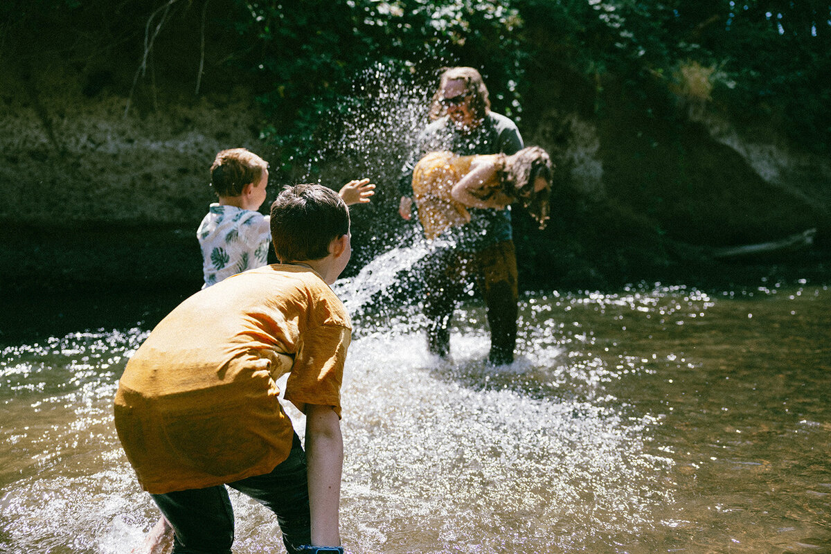 Dad plays joyfully with his kids in the river during the month of August in Oregon. 