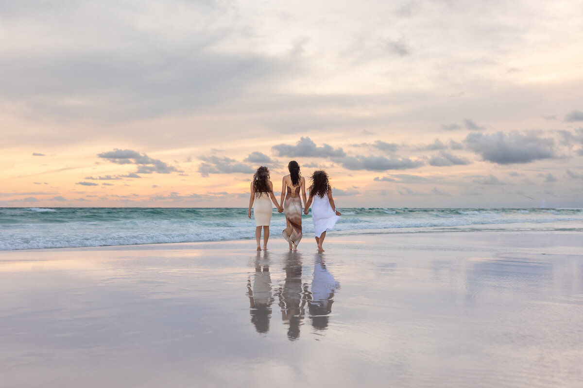 3 sisters walking hand in hand out into the water in front of Adagio on 30a.