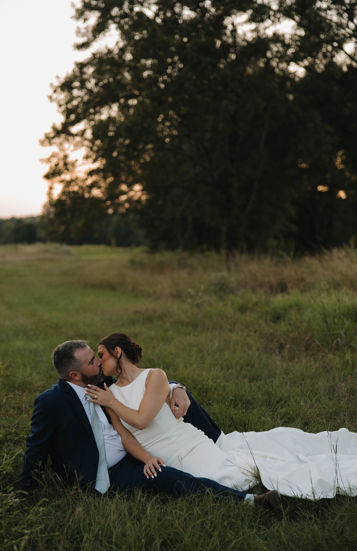 Bride and groom sitting in a grass field kissing in Starkville, MS
