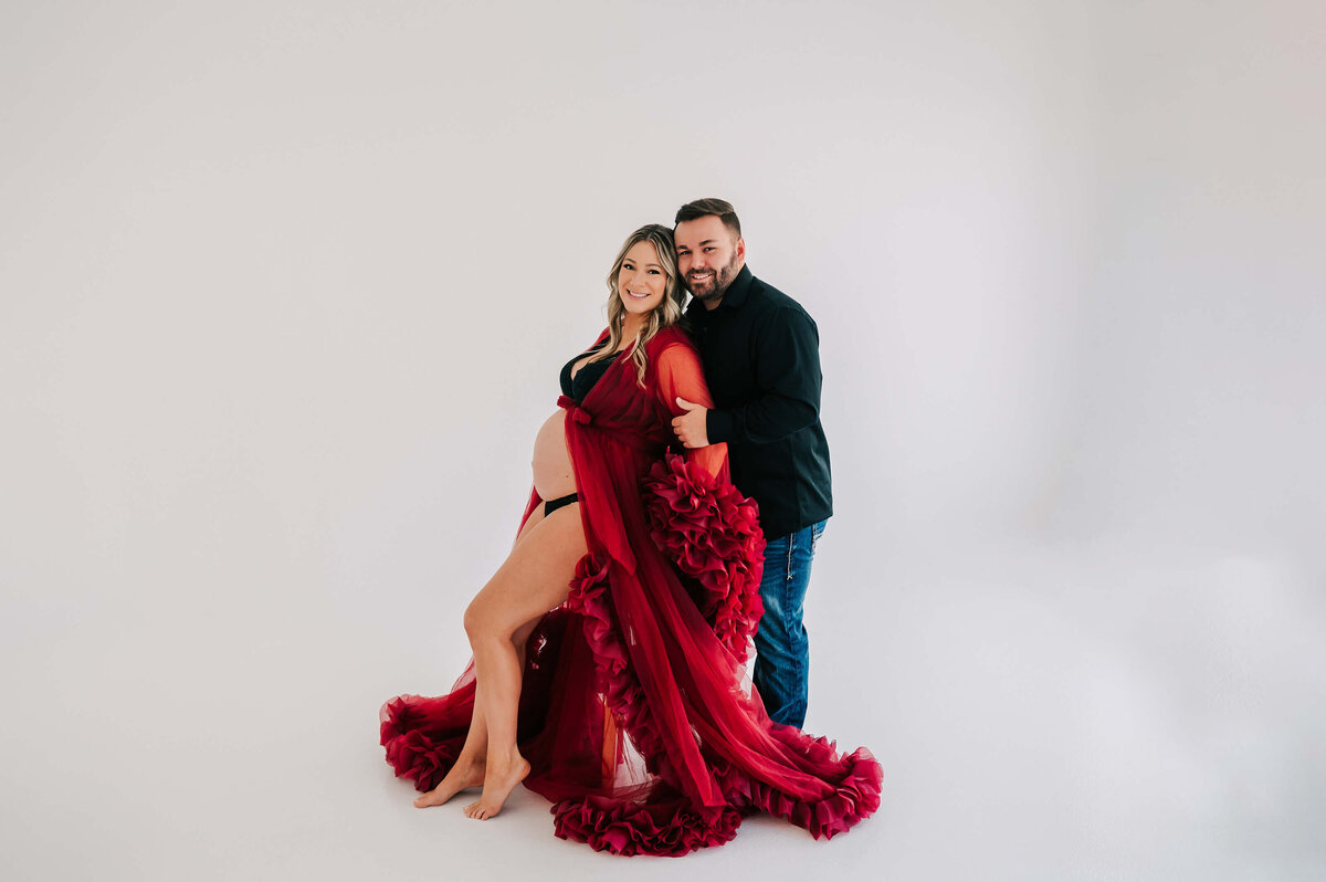 pregnant couple in red robe in maternity photography studio in Joplin MO